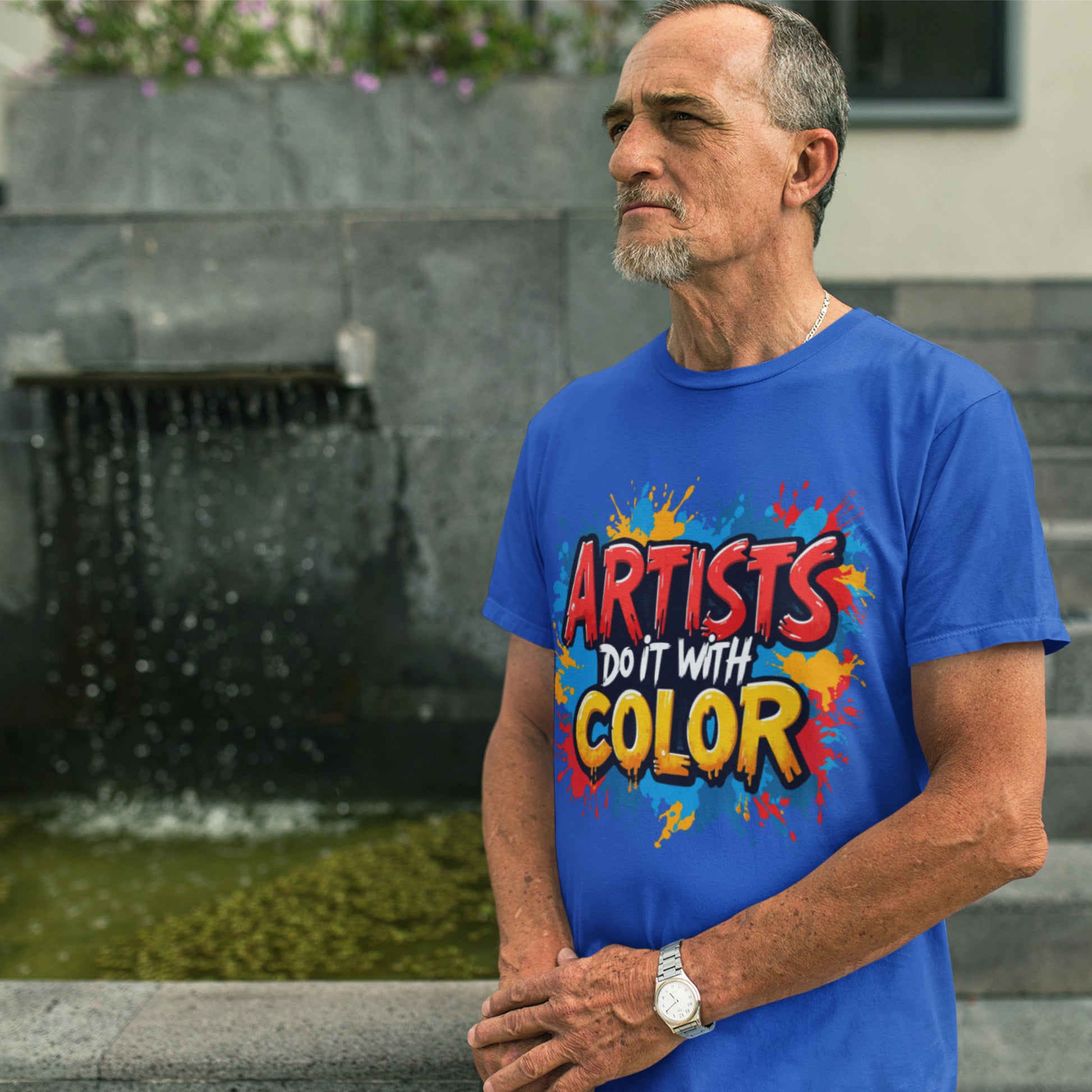 Man wearing a blue t-shirt with colorful text standing in front of a fountain.