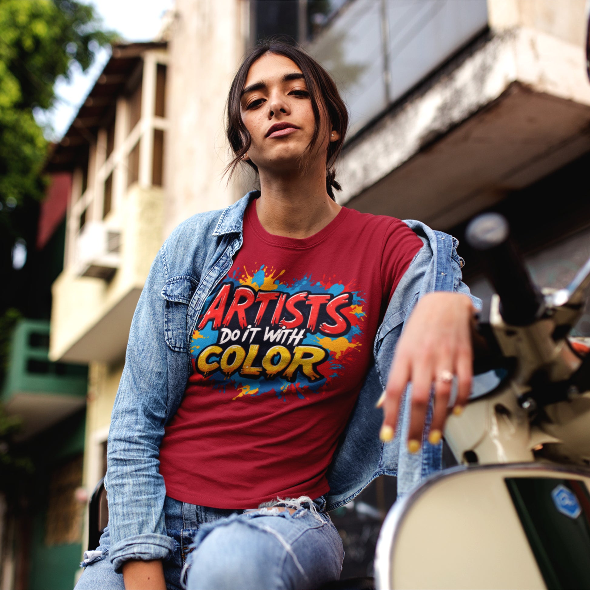Person wearing a red t-shirt with 'Artists Do It With Color' text, standing on a street.