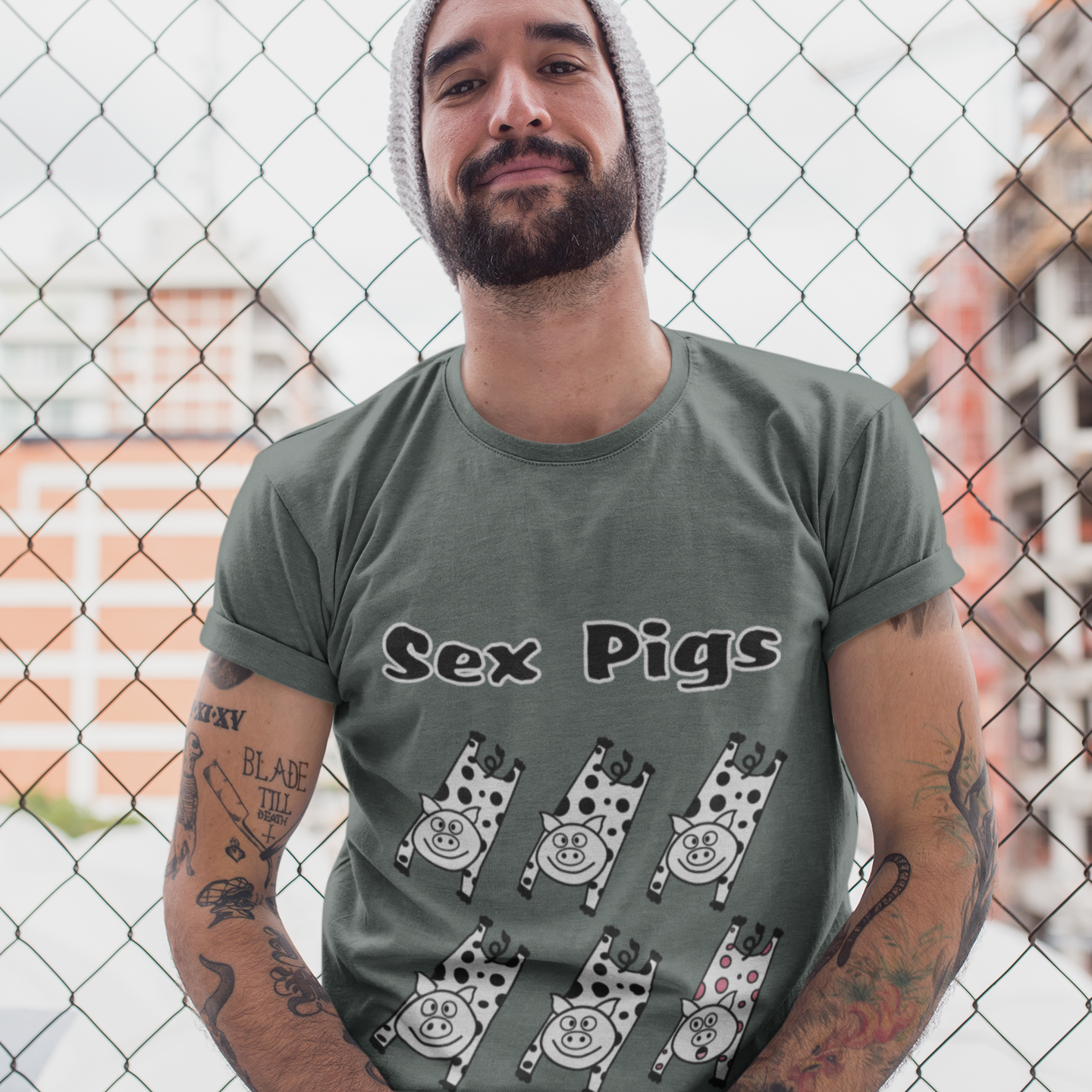 Man wearing a t-shirt with 'Sex Pigs' design in front of a chain-link fence.
