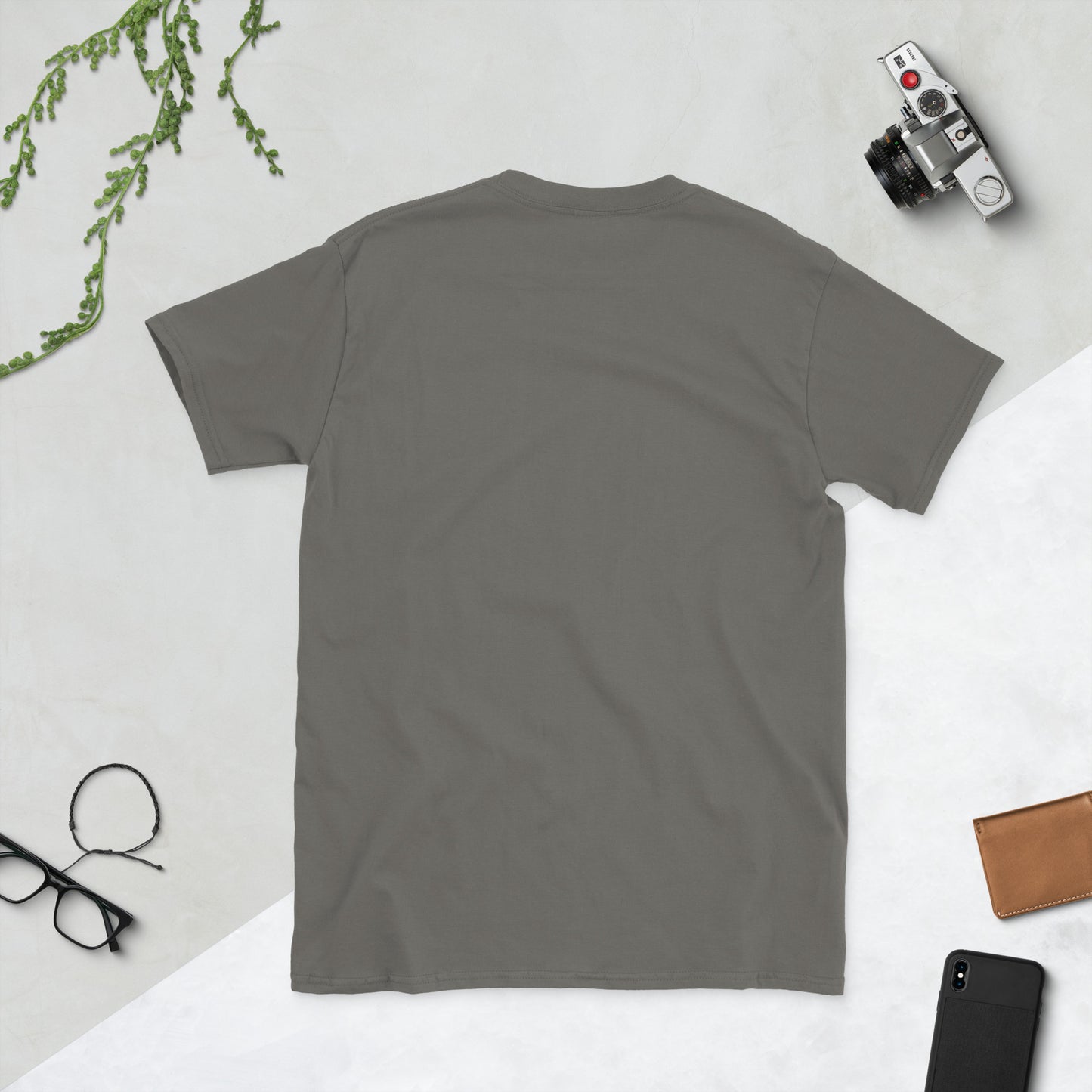 Gray t-shirt on a light gray surface with a camera, phone, and glasses.