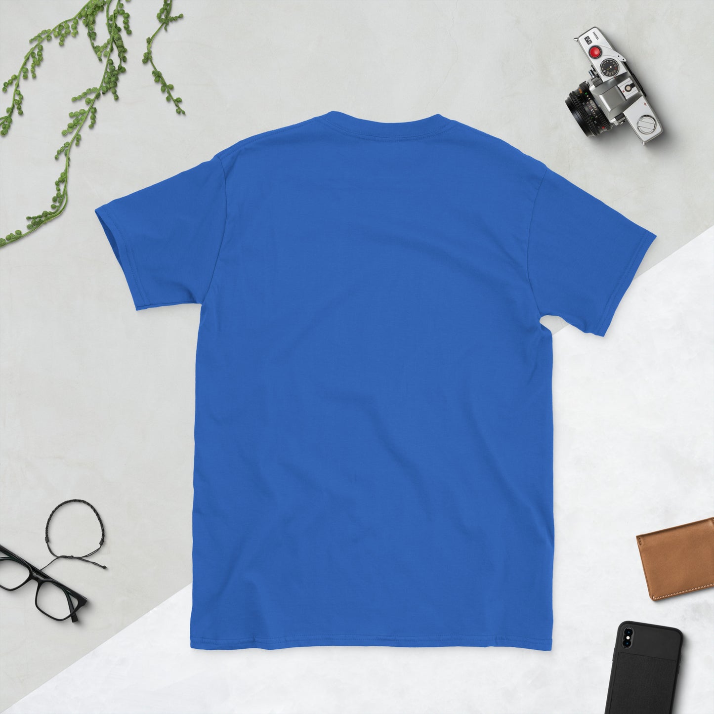 Blue t-shirt on a light gray surface with a camera, phone, and glasses.