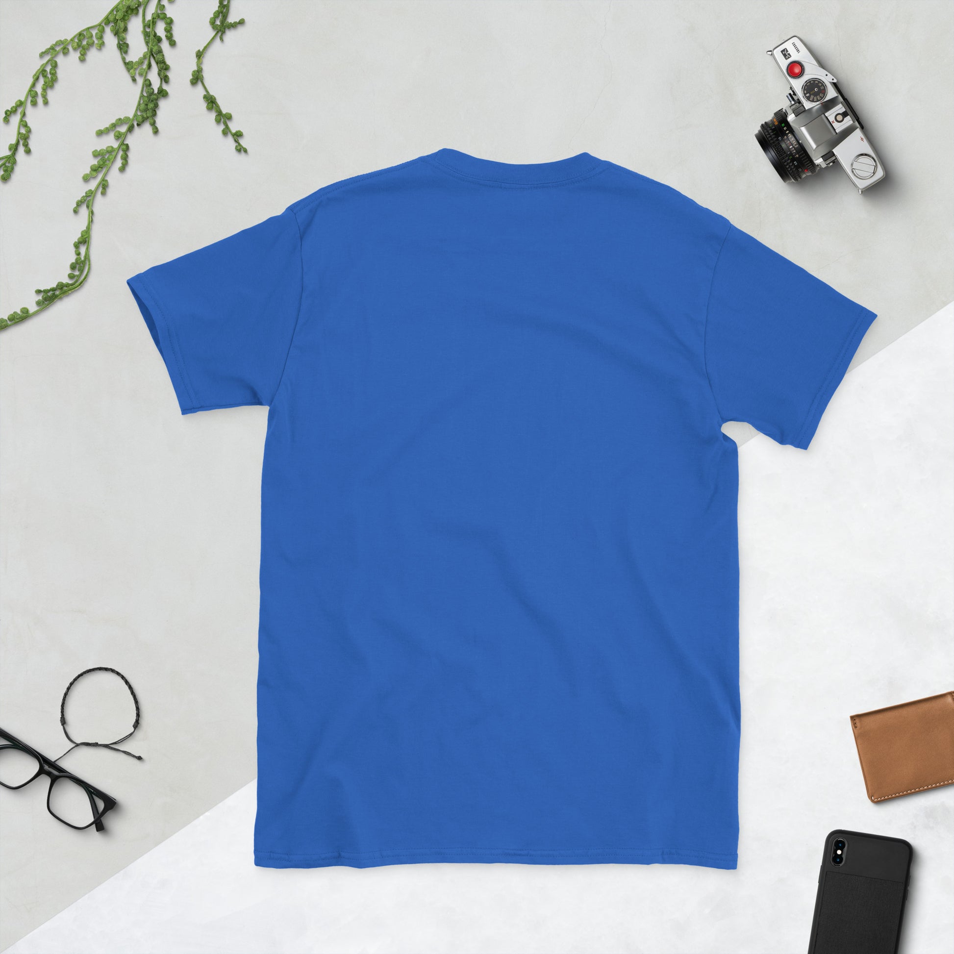Blue t-shirt on a light gray surface with a camera, phone, and glasses.