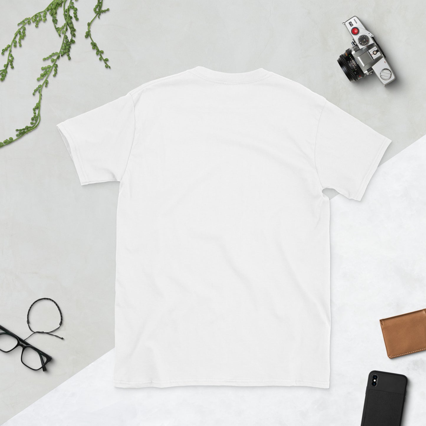 White t-shirt on a light gray surface with a camera, phone, and glasses.